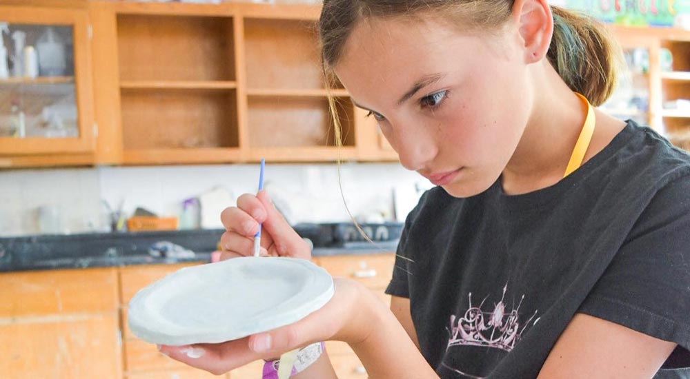 Girl in ceramics class painting a dish
